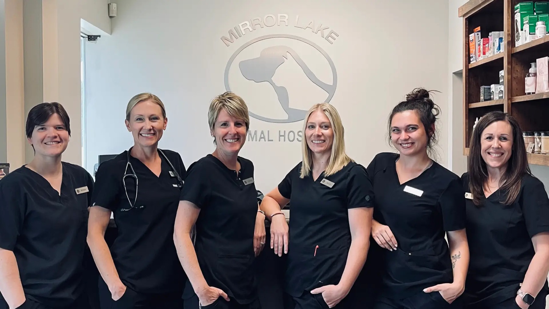 The Mirror Lake Animal Hospital team in scrubs in front of the clinic's logo wall